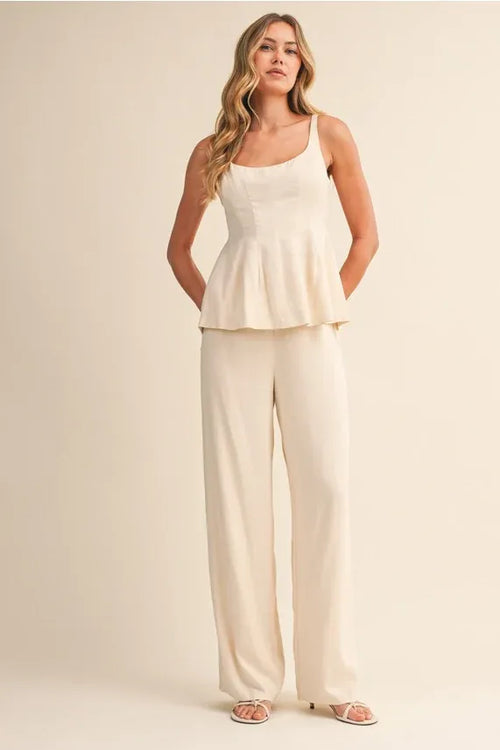 A woman wears a cream scoop neck zipper back blouse with sleeveless peplum and wide-leg trousers elegant outfit