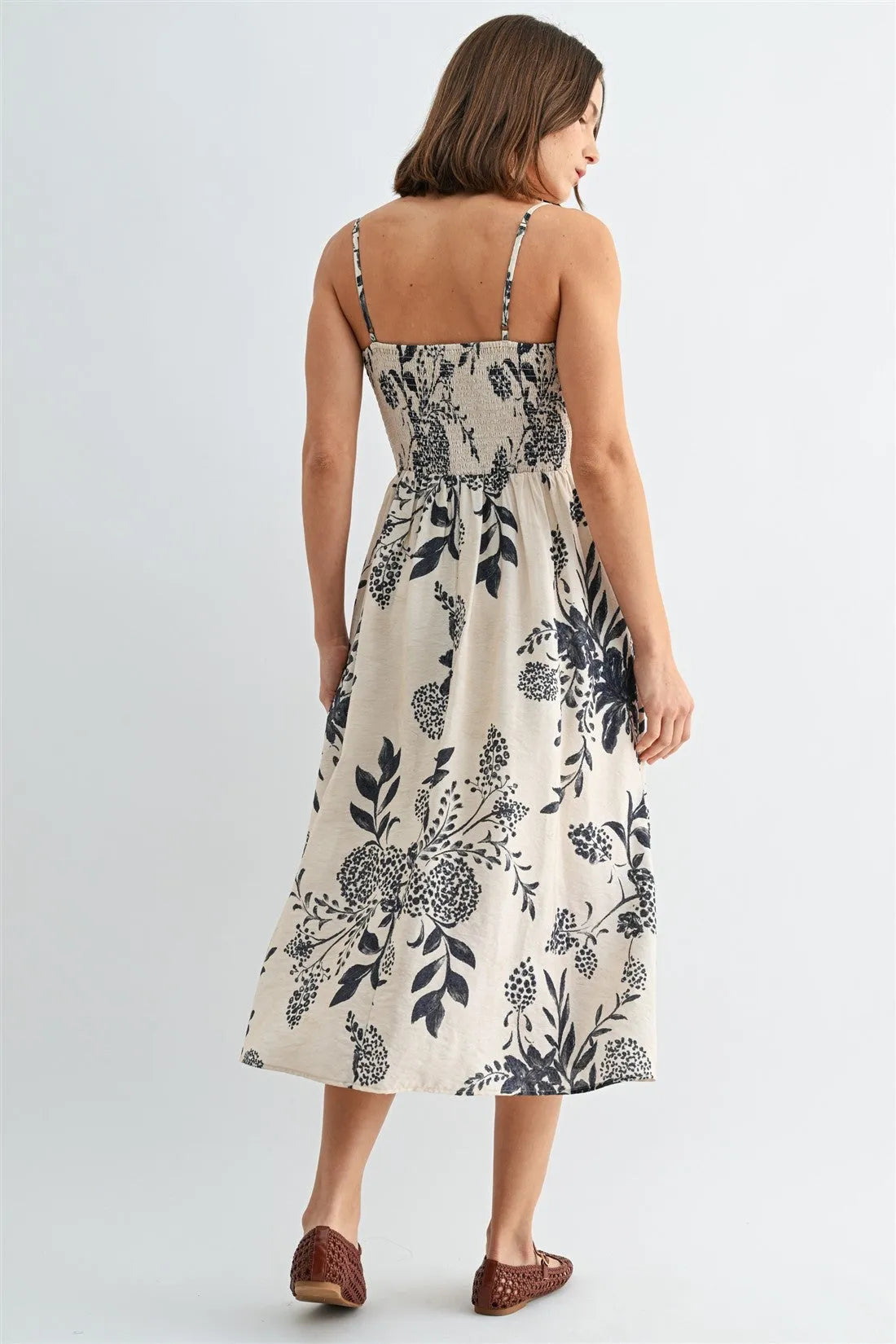A woman wears a cream-colored midi dress with black floral prints and spaghetti straps smock waistband
