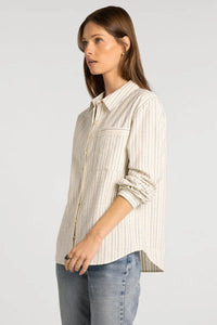 A woman wearing a cream-colored, vertically striped supply Lexington shirt with rolled sleeves and subtle dark pinstripes