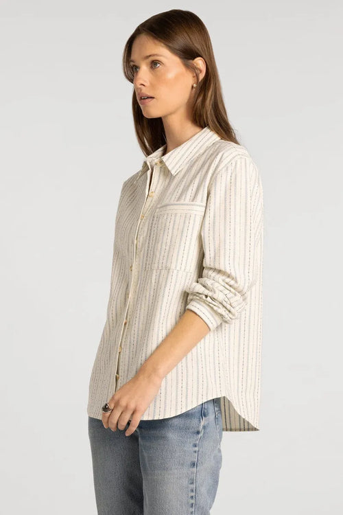 A woman wearing a cream-colored, vertically striped supply Lexington shirt with rolled sleeves and subtle dark pinstripes