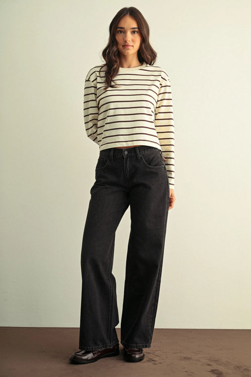 A woman wears low rise baggy wide dark denim jeans paired with a cream and black striped long-sleeved sweater