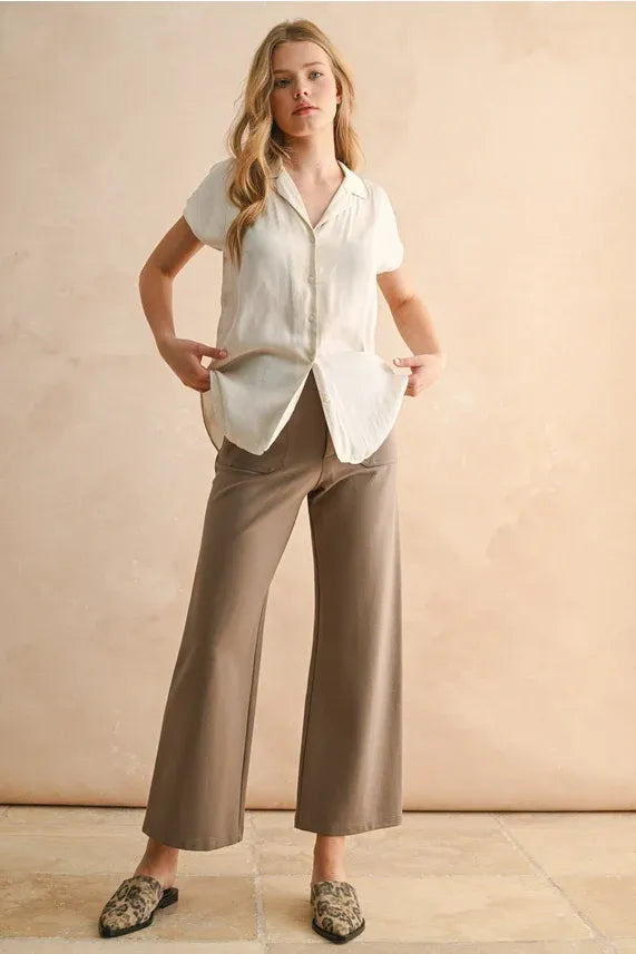 A woman wears a crisp white lightweight button down cap sleeve shirt with relaxed fit and pleated hem details