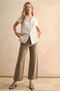 A woman wears a crisp white lightweight button down cap sleeve shirt with relaxed fit and pleated hem details