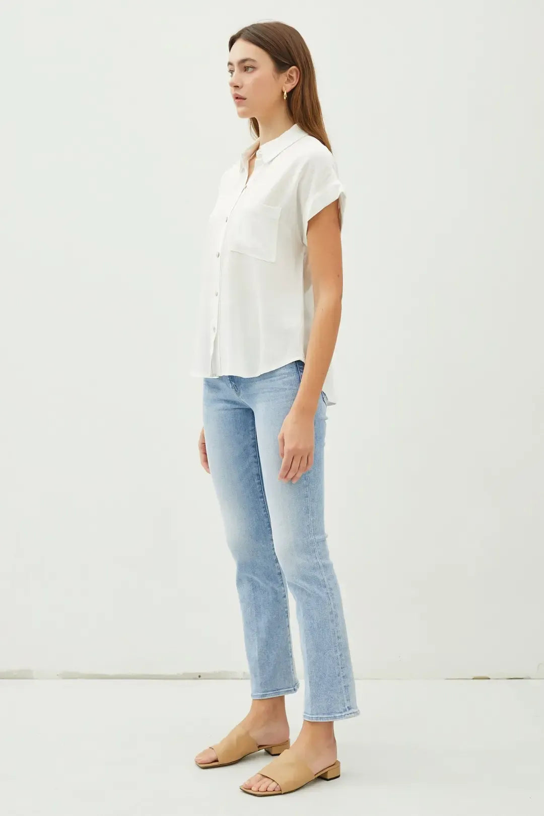 A woman wears a solid short sleeve white button down shirt with collar and chest pocket paired with light-wash jeans