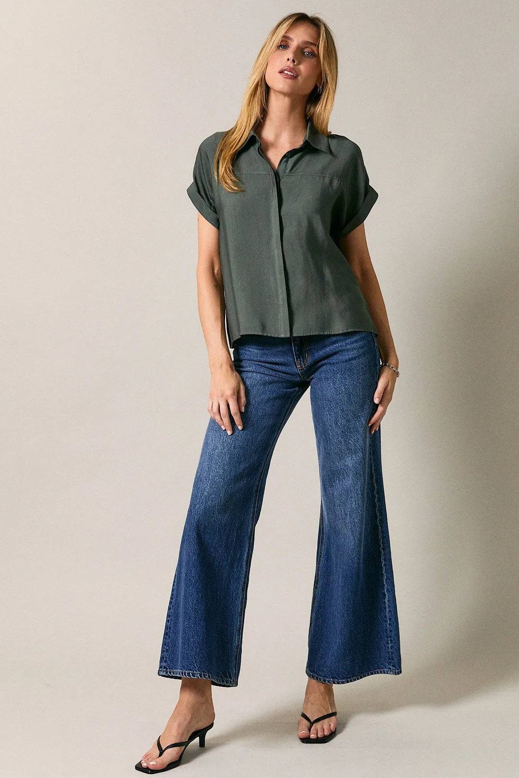 A woman wears a dark olive green collard wide shoulder button down shirt with relaxed fit and wide-leg denim jeans