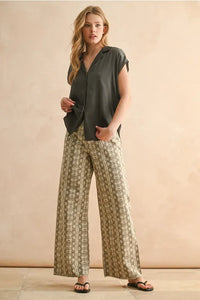 A woman wears a dark olive green lightweight button cap sleeve shirt with wide-leg beige and brown snake print pants