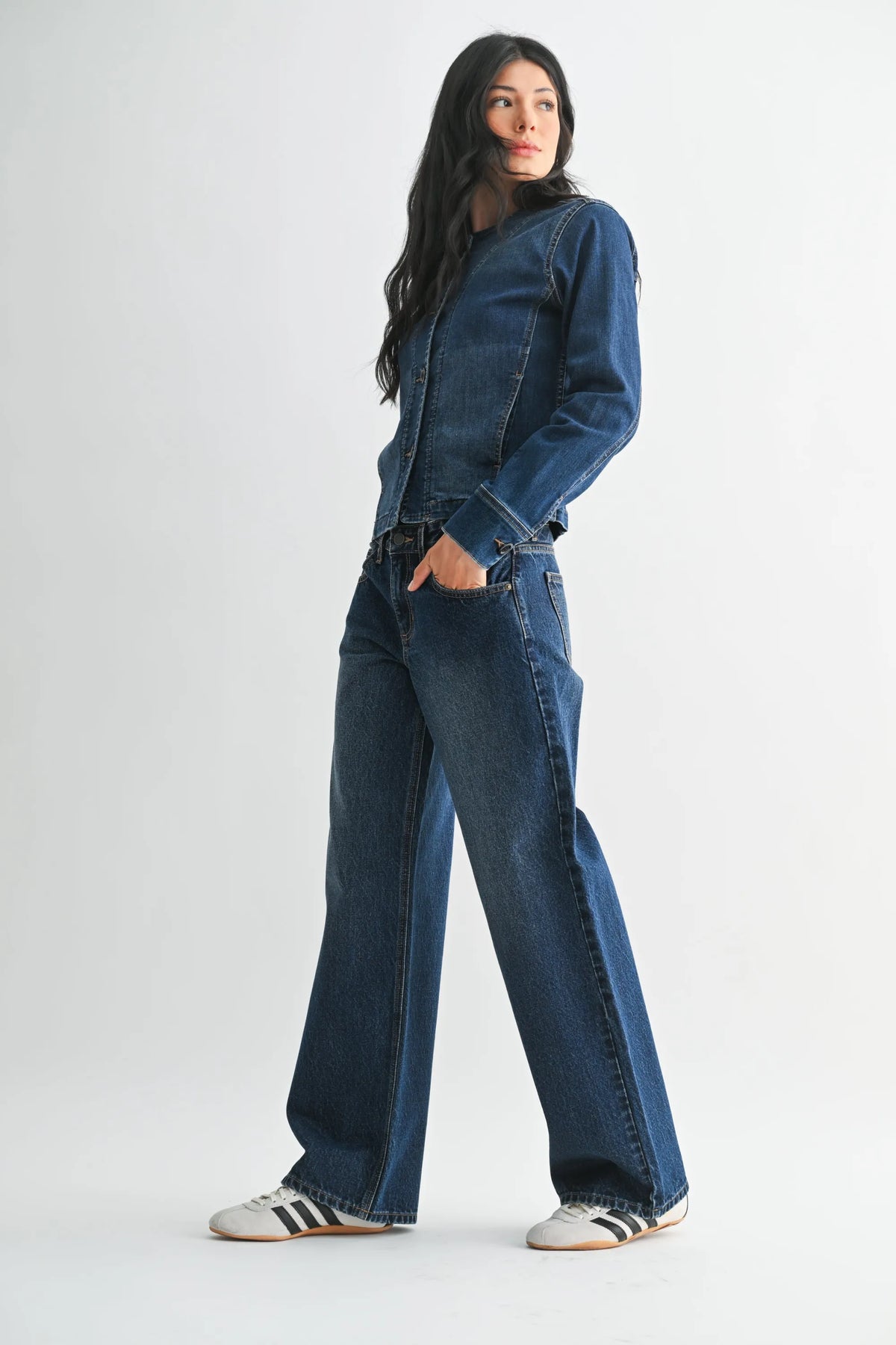 A woman wears dark blue low rise baggy wide denim jeans paired with a matching denim jacket and white sneakers