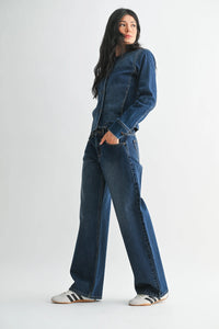 A woman wears dark blue low rise baggy wide denim jeans paired with a matching denim jacket and white sneakers