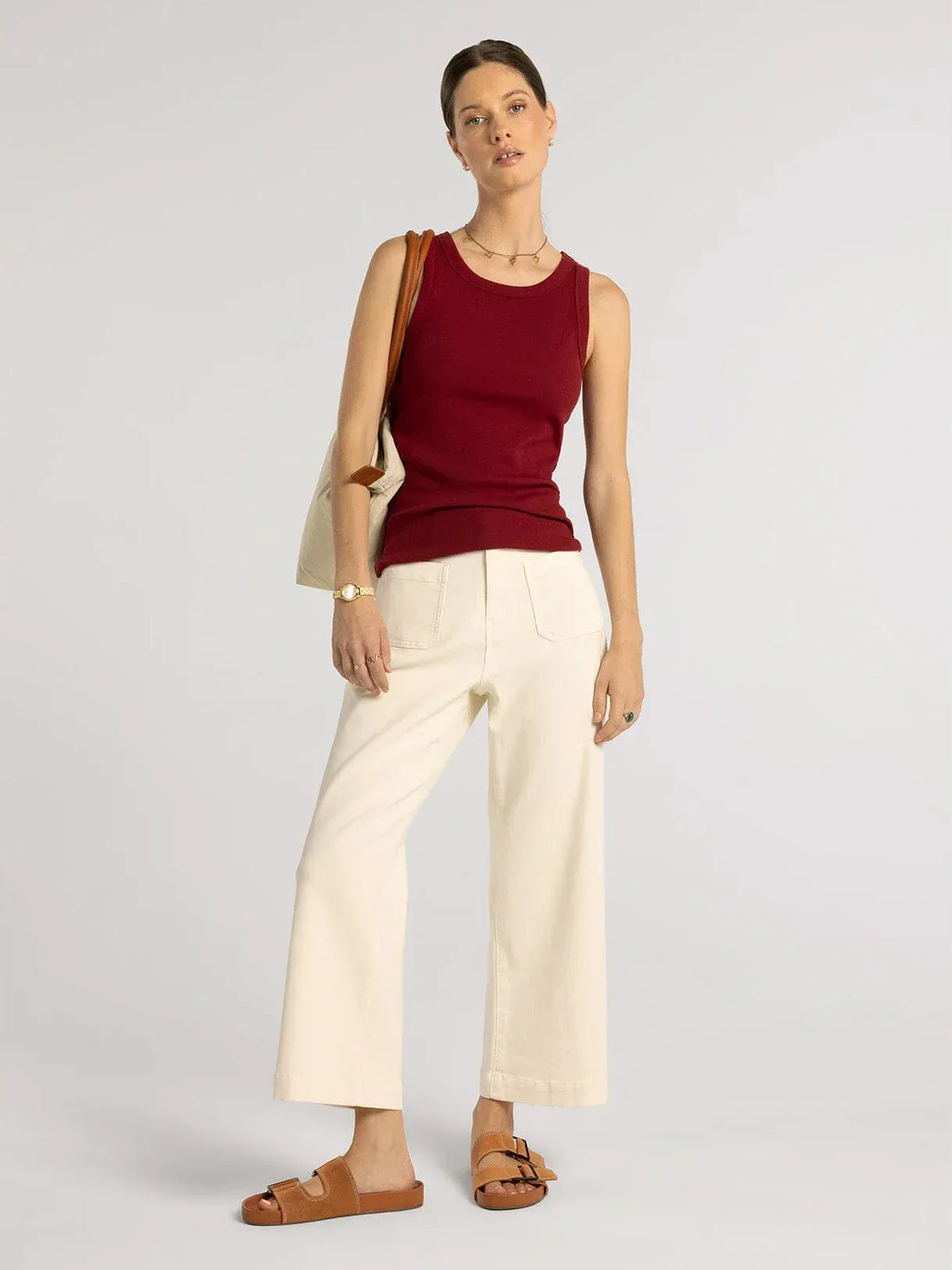 A woman wearing a fitted ribbed burgundy sleeveless edlin basic tank with a rounded neckline from Thread and Supply