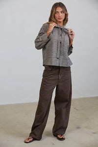 A woman wears a gray and black plaid bow tied collar shirt with long sleeves and a button-down front