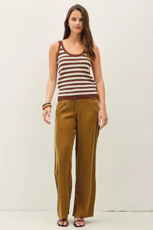 A woman wears a textured stripe tank sweater in brown and cream knitted fabric paired with olive green satin trousers