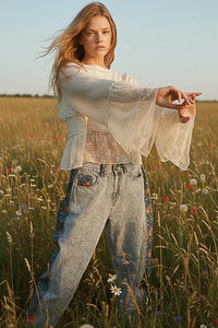 A woman wearing an off-white lace ruffle blouse with round neck flared sleeves and high-waisted embroidered jeans