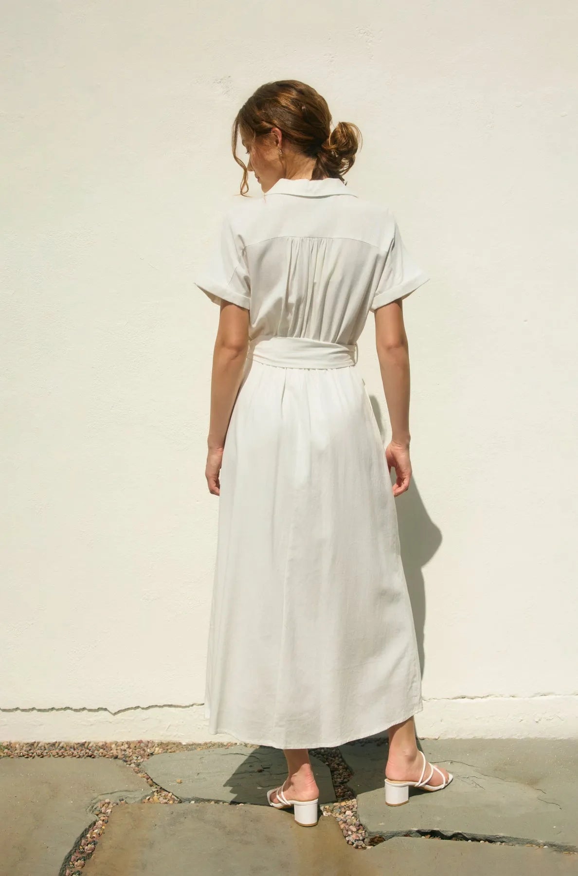 A woman wears a light gray belted midi dress with collar and pleats showcasing the wicker buckle maxi dress