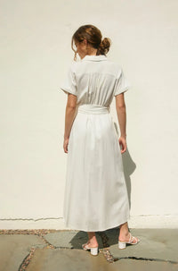 A woman wears a light gray belted midi dress with collar and pleats showcasing the wicker buckle maxi dress