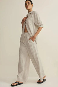 A woman wears light gray and white henri striped wide linen pants paired with a matching loose striped wide leg shirt