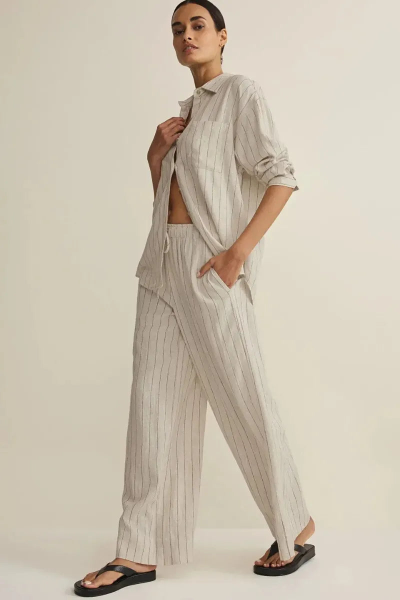A woman wears light gray and white henri striped wide linen pants paired with a matching loose striped wide leg shirt