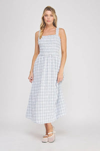 A woman wearing a light blue and white plaid print smocked midi dress with sleeveless square neckline design
