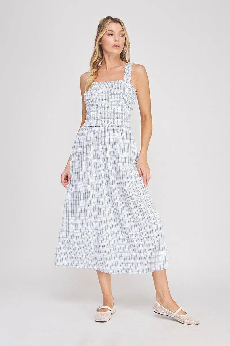 A woman wearing a light blue and white plaid print smocked midi dress with ruffled shoulder straps
