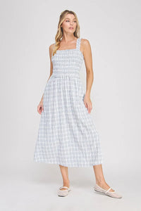 A woman wearing a light blue and white plaid print smocked midi dress with ruffled shoulder straps