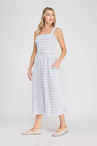 A woman wearing a light blue and white plaid print smocked midi dress with ruffled straps and side pockets