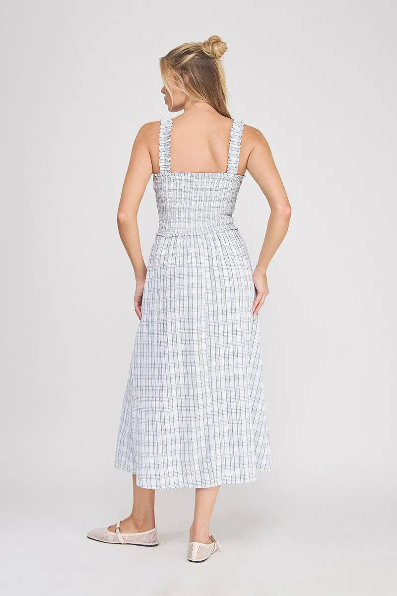 A woman wearing a light blue and white plaid print smocked midi dress with ruffled shoulder straps