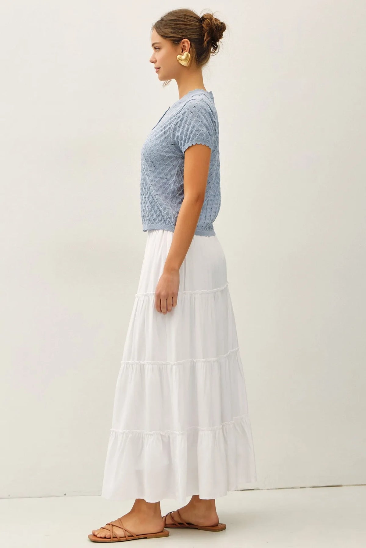 A woman wears a light blue pointelle stitch short sleeve cardigan with an intricate pattern paired with a white skirt