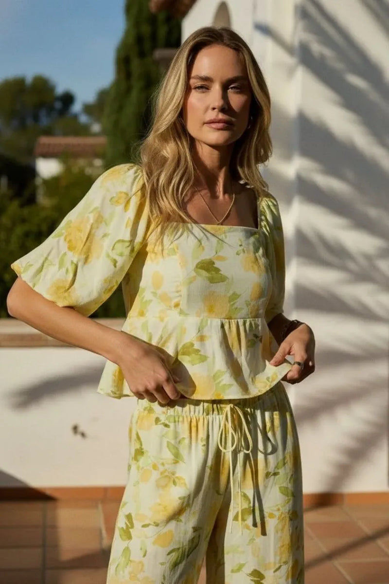 A woman wears a light yellow floral print square neck bubble hem peplum blouse with puffy sleeves and drawstring pants