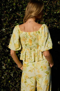 A woman wearing a light green and yellow floral print square neck bubble hem peplum blouse with puffed sleeves and smocked back