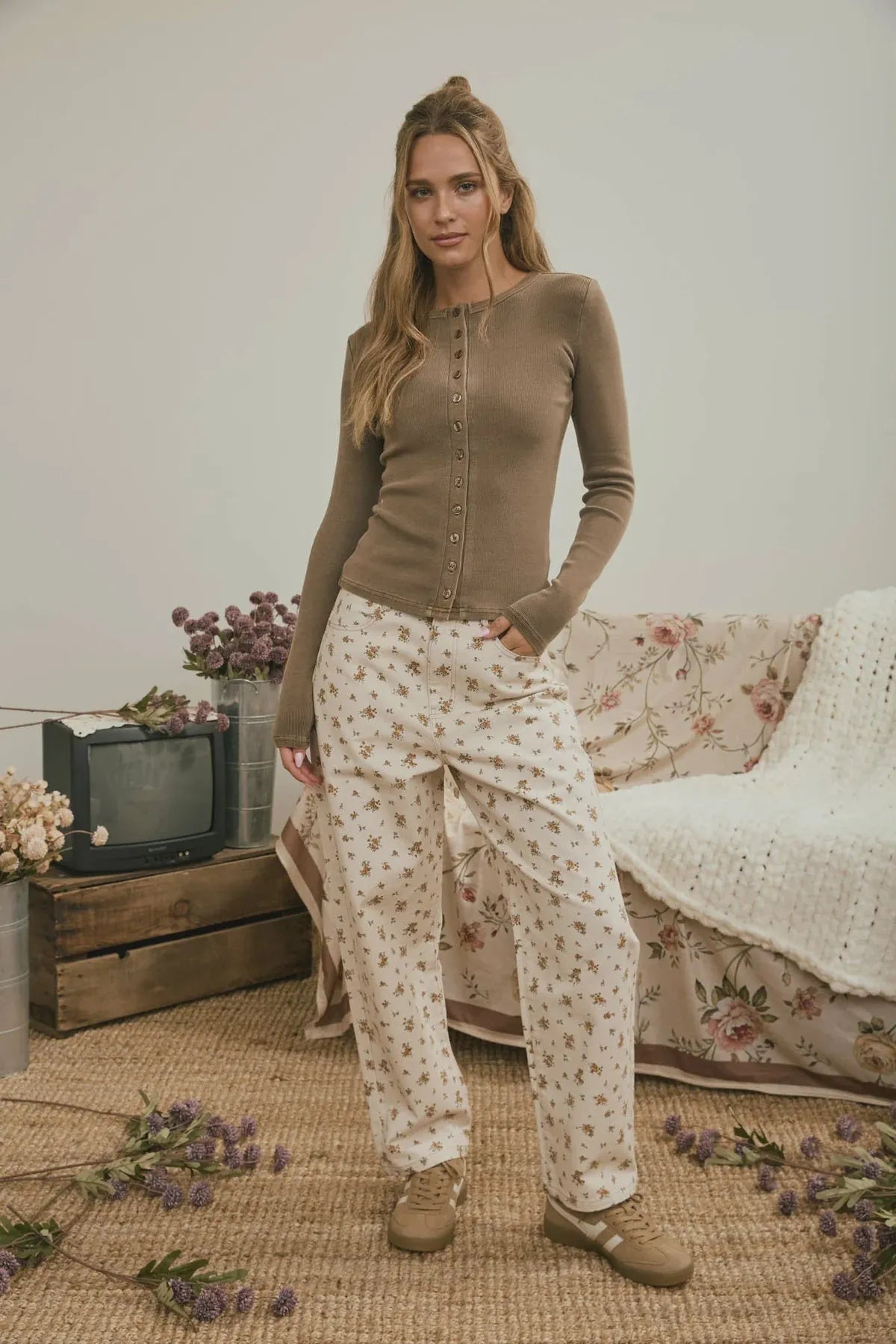 A woman wearing floral denim pattern jeans in off-white with delicate floral prints paired with an olive green cardigan