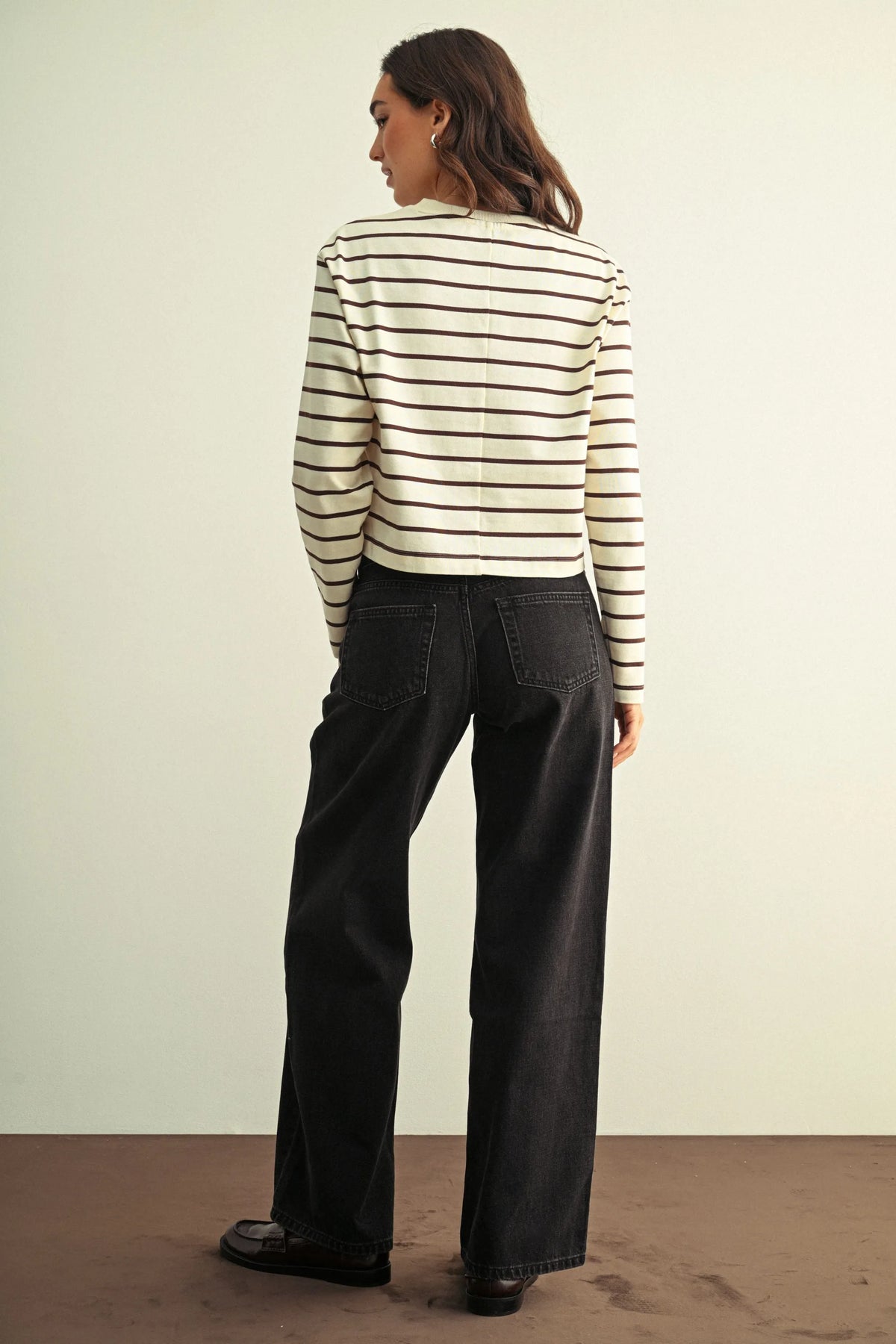 A woman wearing a cream and black striped knit top paired with low rise baggy wide leg denim jeans