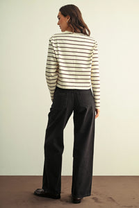 A woman wearing a cream and black striped knit top paired with low rise baggy wide leg denim jeans