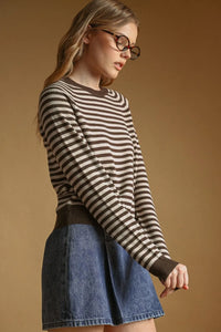 A woman wearing a beige and dark brown striped round neck sweater paired with a blue denim skirt