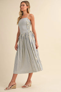 A woman wears a navy and white striped midi dress with spaghetti straps a corset lace-up front and a gathered waist