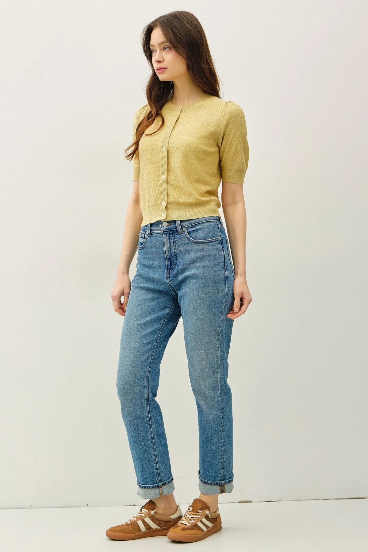 A woman wearing a mustard-yellow pointelle puff sleeve cardigan with button closures and subtle embroidery