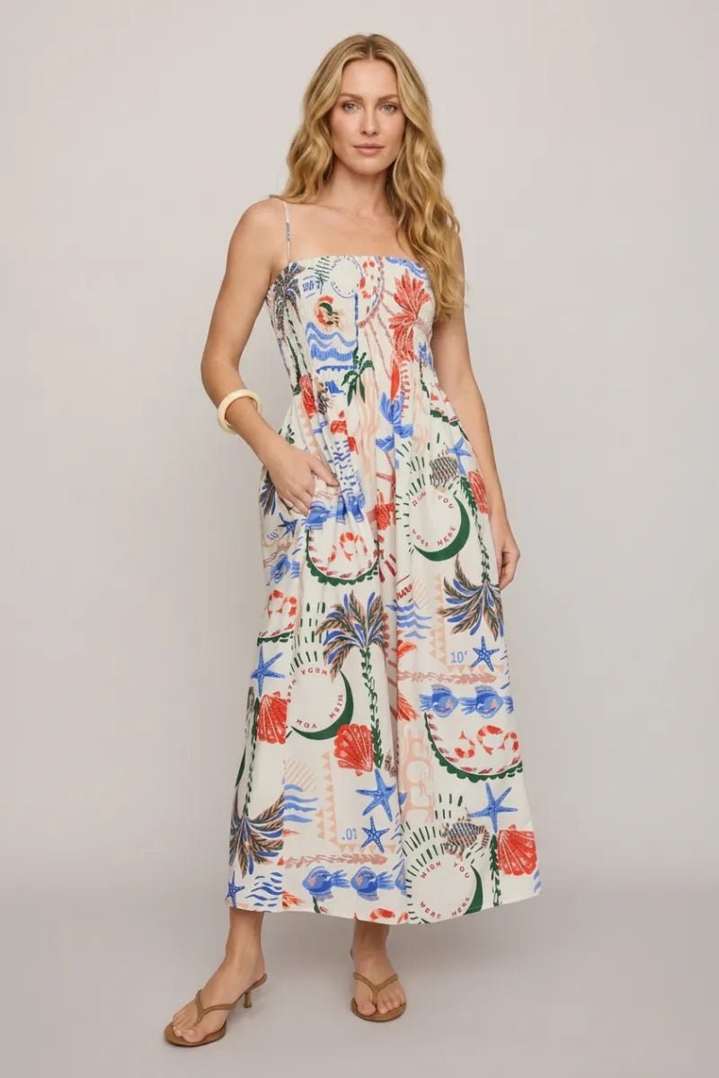A woman wears the cornelia getaway maxi dress in off-white with vibrant tropical and nautical patterns