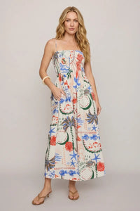 A woman wears the cornelia getaway maxi dress in off-white with vibrant tropical and nautical patterns