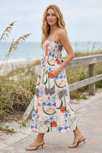A woman wears a flowing off-white getaway maxi dress with vibrant blue starfish red coral and green palm fronds pattern