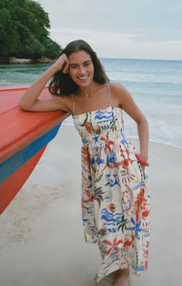 A woman wears a flowing off-white cornelia getaway maxi dress with vibrant red blue and green tropical patterns