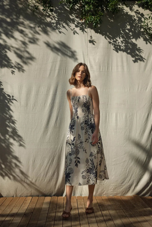 A woman wears an off-white midi dress with delicate black floral embroidery and spaghetti straps smock detailing