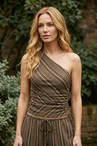 A woman wears a brown striped asymmetrical one shoulder ruched top with matching high-waisted pants in women’s boho chic clothing