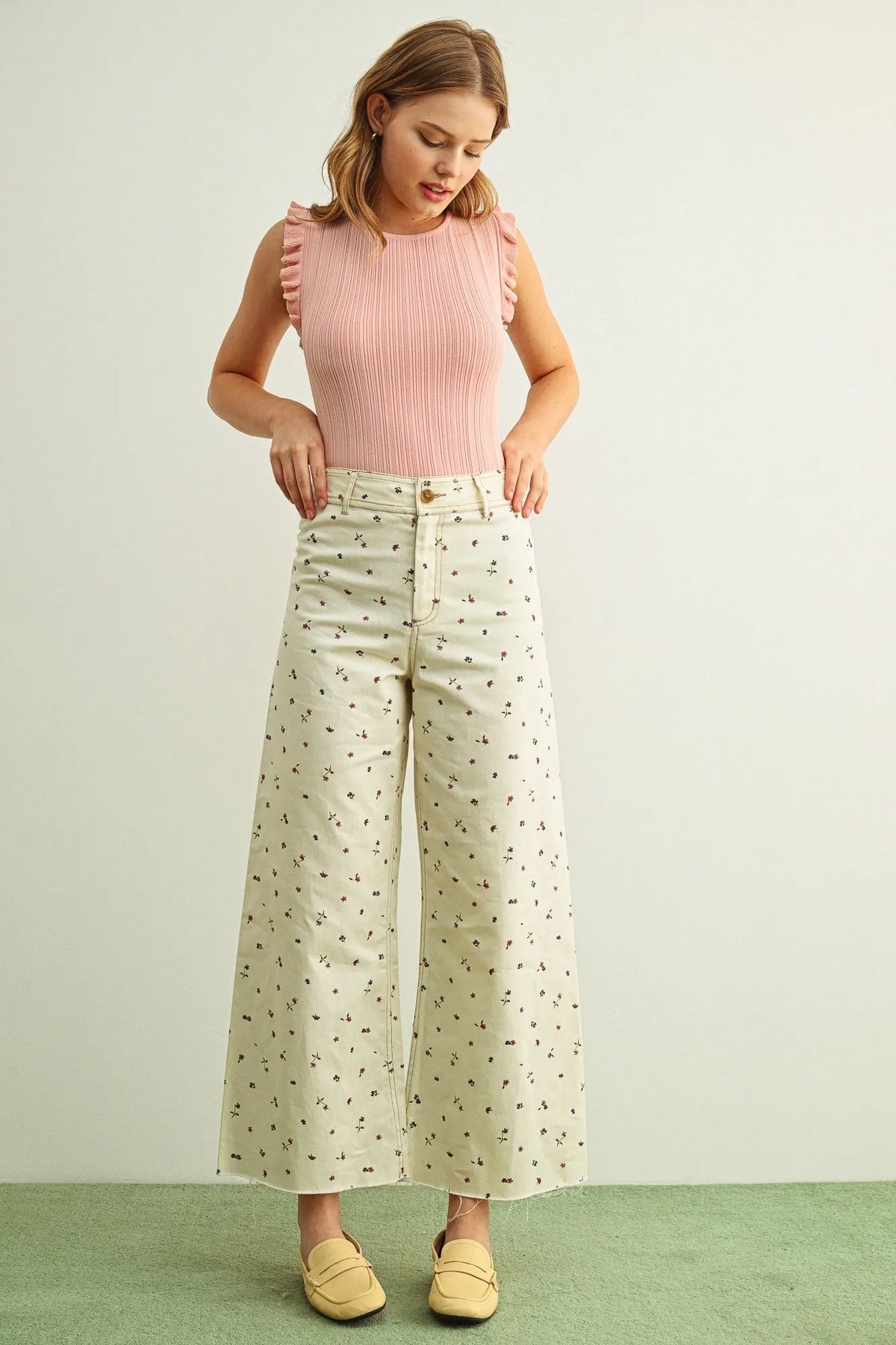 A woman wearing multi color floral print stretched wide-leg pants paired with a pink ribbed sleeveless top with ruffled shoulders