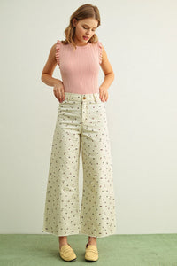 A woman wearing multi color floral print stretched wide-leg pants paired with a pink ribbed sleeveless top with ruffled shoulders