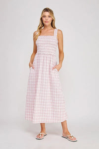 A woman wears a pink and white plaid print smocked midi dress with square neckline and side pockets