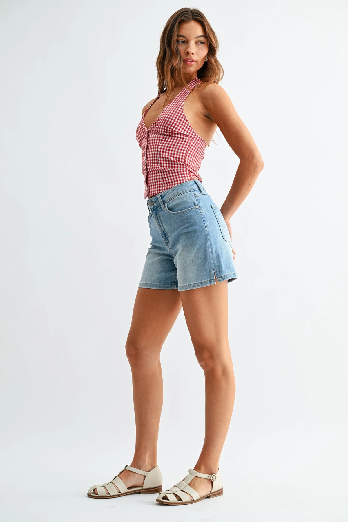 Woman in mid rise walking denim shorts with slit and gingham halter top
