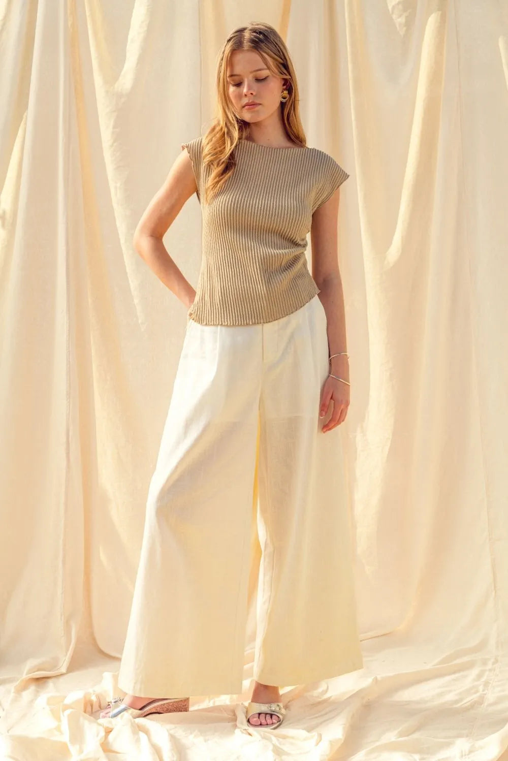A woman wears a beige crinkled fabric shirring cap sleeve top paired with wide-leg cream trousers