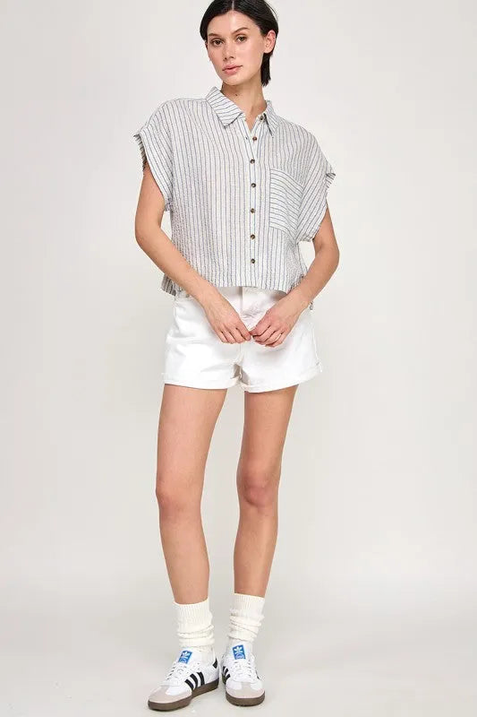 A woman wears a cap sleeve striped button down shirt with vertical gray and white stripes in short sleeves