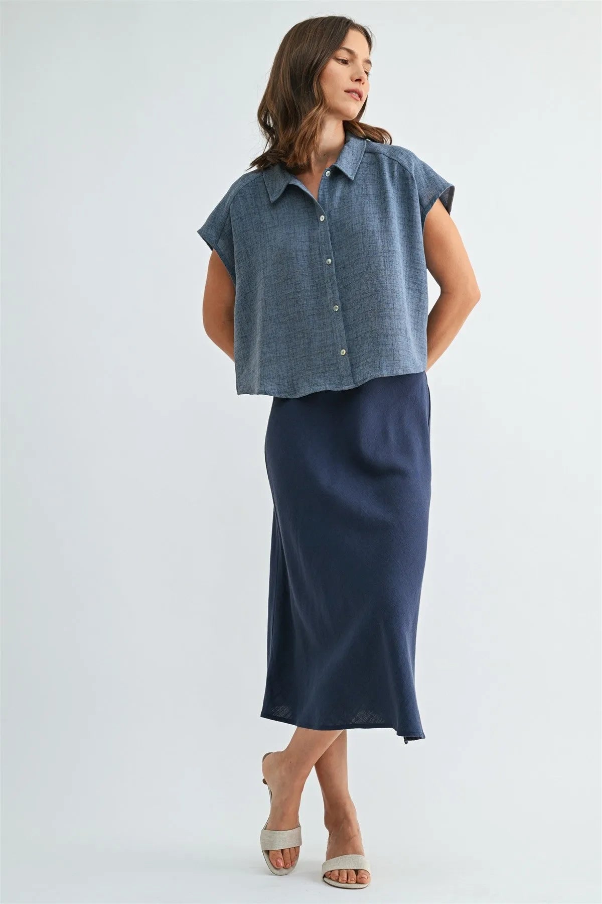 A woman wears a textured denim blue dolman sleeve button shirt paired with a navy silk midi skirt