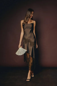 A woman wears a dark olive satin slip dress with asymmetrical lace trim featuring intricate black lace detailing