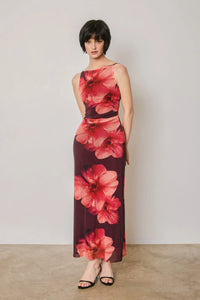 A woman wears a sleeveless floral mesh open back maxi dress with bold red floral patterns on deep burgundy fabric