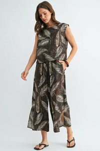 A woman wears a dark brown sleeveless leaf print wide jumpsuit with white feather patterns and wide-leg pants